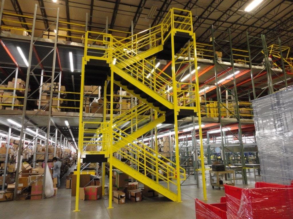 woman behind OSHA yellow steel stairway with dark hair and gray jumpsuit working with boxes in e-commerce shipping facility